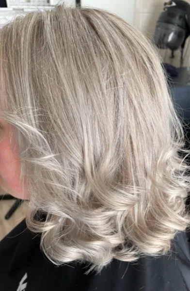 Deze dame met schouderlang haar heeft gekozen voor een platinablond haarkleur met highlights en lowlights om het platinablond een mooie natuurlijke look te geven. Als styling heeft Leonie mooie golvende krullen gemaakt.